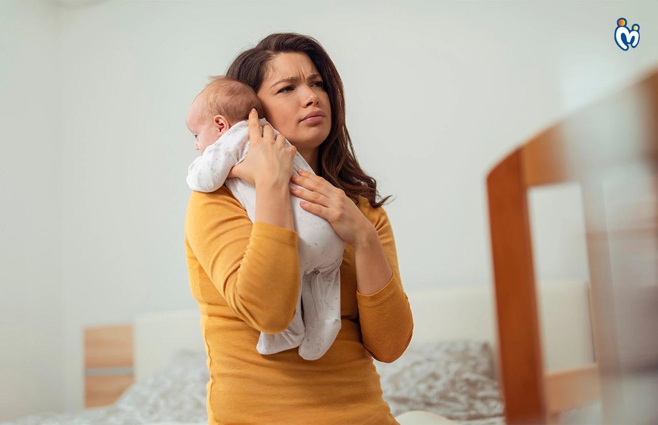 Tired young mother holding crying baby in bedroom